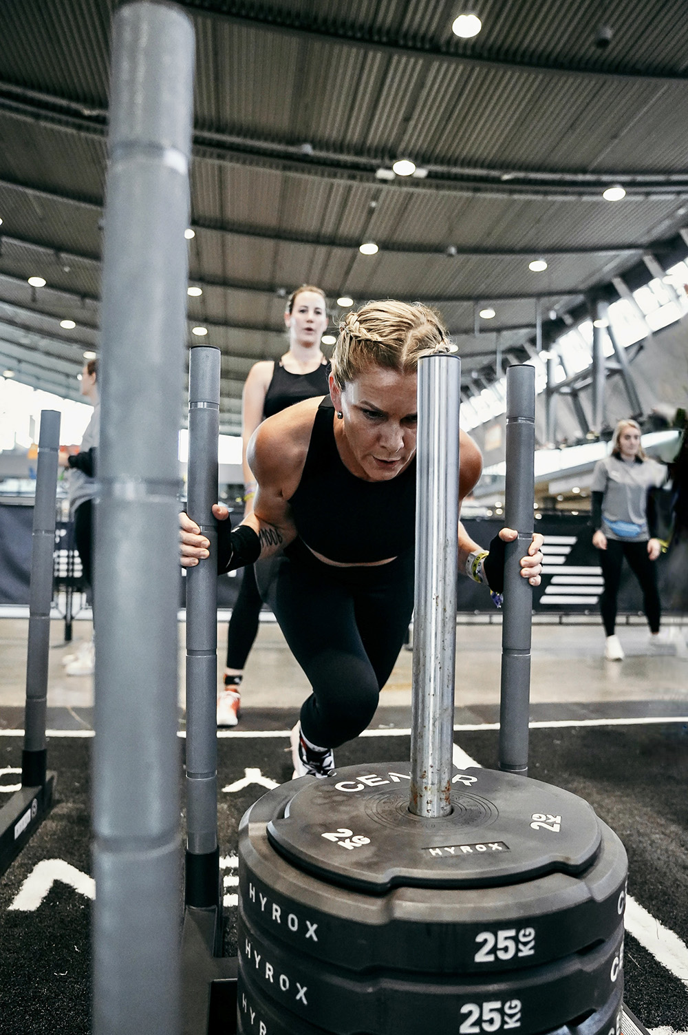Athletin schiebt einen schweren HYROX Schlitten mit 25kg Gewichten beim Wettkampf
