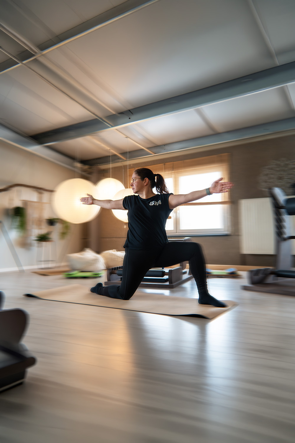 Trainerin in Warrior Pose bei einer Mobility Session im warm beleuchteten Studio