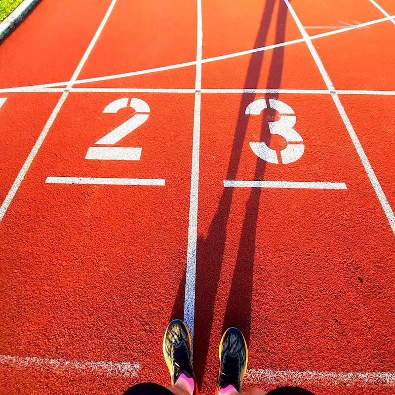 Rote Tartanbahn mit Startnummern 2 und 3, Laufschuhe eines Athleten sichtbar