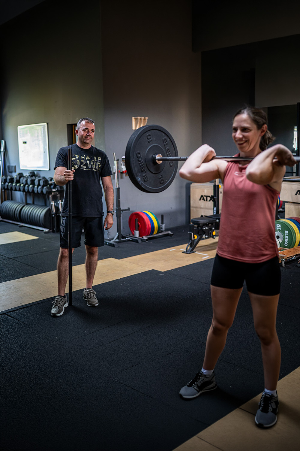 Trainer beobachtet Athletin beim Front Rack Hold mit Langhantel in der Halle Zwo