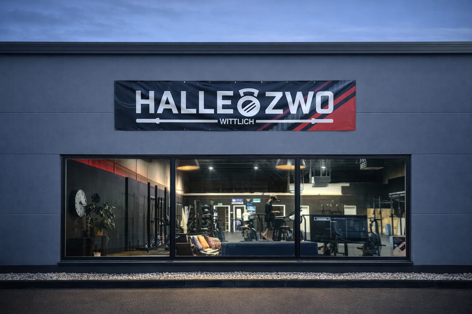 Beleuchtete Außenansicht des Halle Zwo Fitnessstudios in Wittlich mit Einblick in den Trainingsbereich am Abend