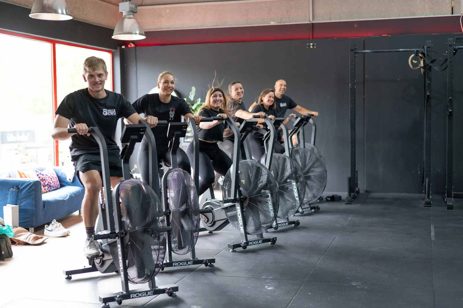 Lächelnde Trainingsgruppe auf Rogue Air Bikes beim Cross Functional Workout in der Halle Zwo Wittlich